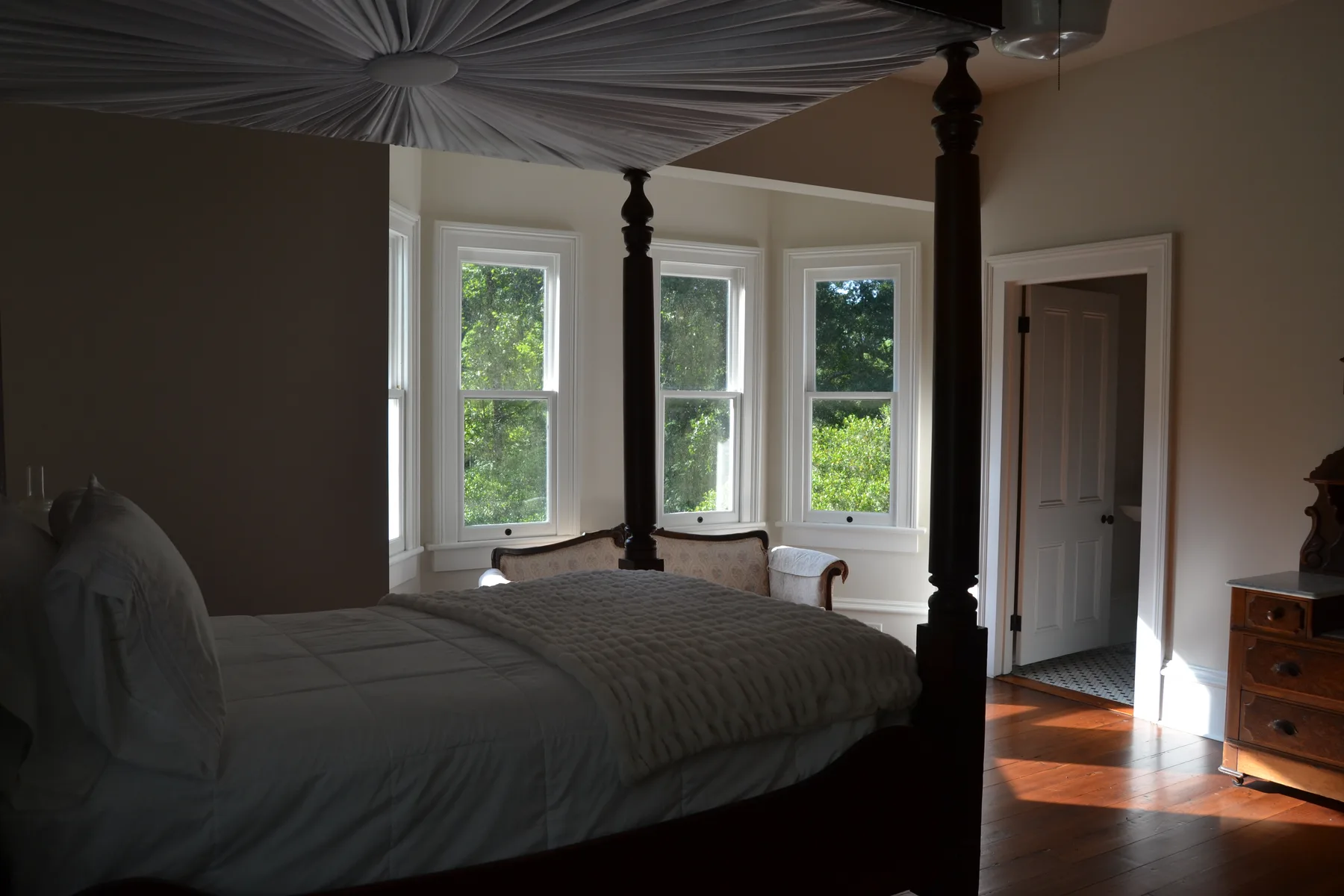 A light-filled guest bedroom with tall windows over the grounds