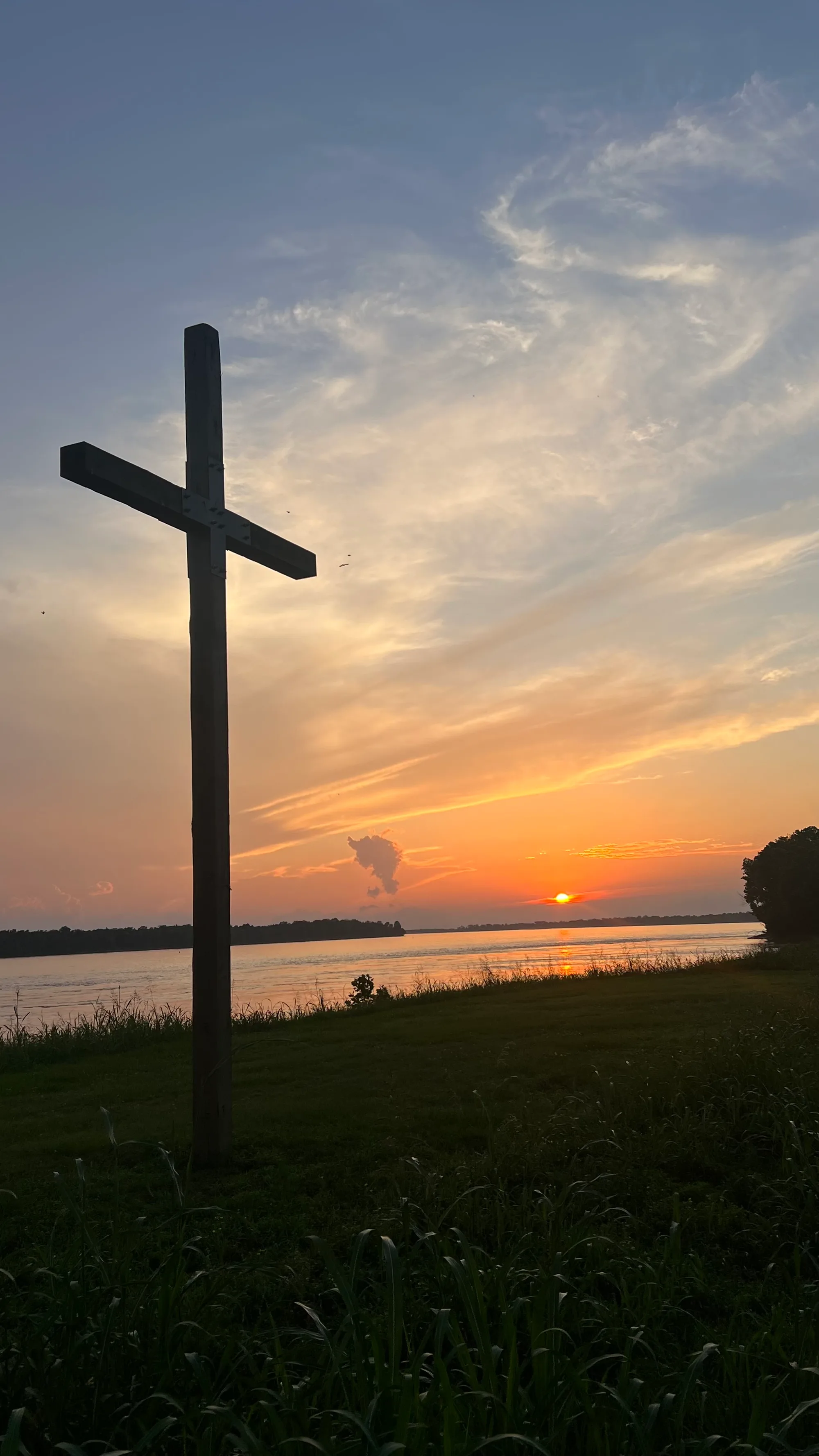 A cross silhouetted against sunset over the Mississippi River